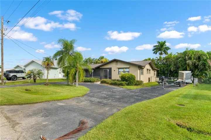 Paved driveway with ample parking, mature palm trees, and established landscaping