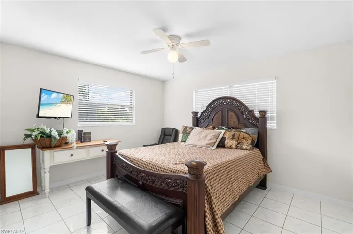 White tiled flooring, dual windows with blinds, ceiling fan with integrated lighting, and a wall-mounted television