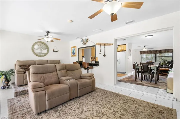 White tile flooring, ceiling fans with integrated lighting, a built-in breakfast bar, and an open doorway to an additional room