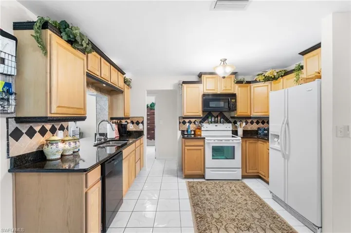 Kitchen featuring wood cabinetry, black countertops, tile backsplash with accent tiles, a double basin sink, and white tile flooring