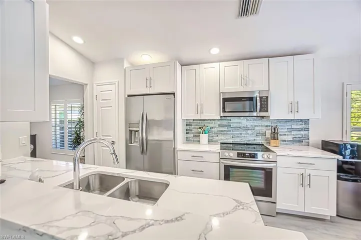 Kitchen featuring stainless steel appliances, light stone countertops, white cabinetry, and recessed lighting