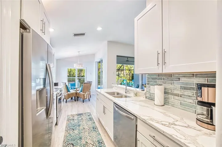 Kitchen featuring stainless steel appliances, lofted ceiling, light stone counters, light wood-style floors, and healthy amount of natural light