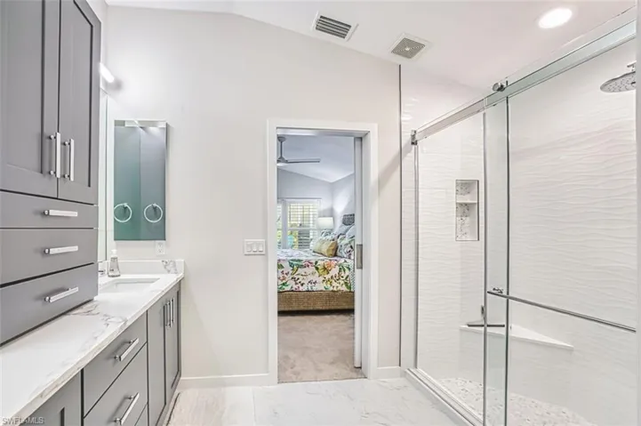 Ensuite bathroom featuring vaulted ceiling, vanity, a shower stall, and light marble finish flooring