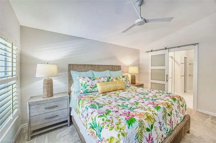 Bedroom featuring lofted ceiling, a barn door, light colored carpet, ensuite bath, and a ceiling fan