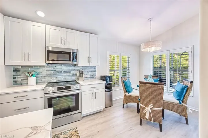 Kitchen with stainless steel appliances, white cabinets, light wood-type flooring, decorative backsplash, and light stone counters