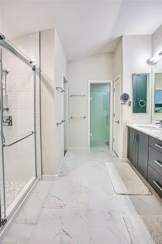 Bathroom featuring a stall shower, vanity, light marble finish flooring, and lofted ceiling