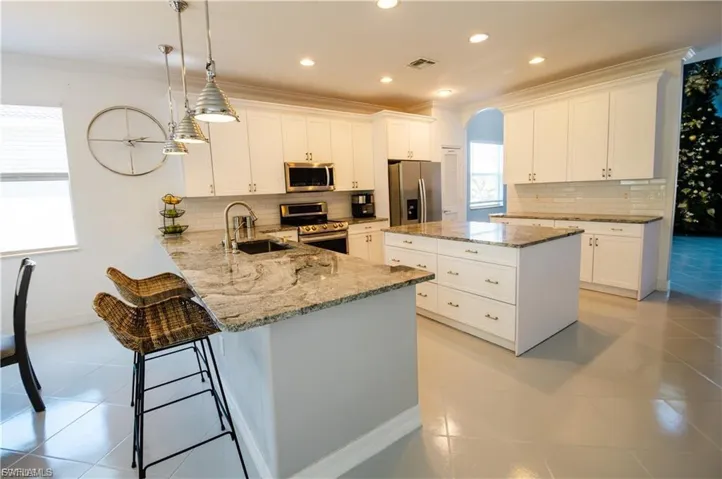 Kitchen with light stone countertops, a peninsula, decorative backsplash, a center island, and crown molding