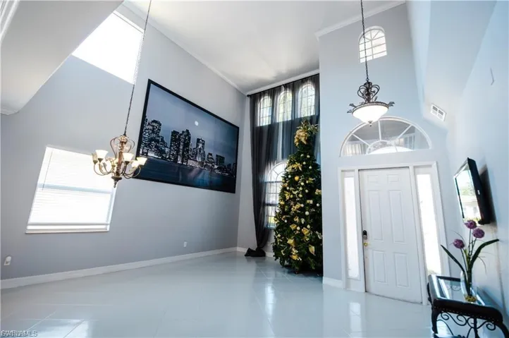 Tiled foyer entrance featuring a chandelier, plenty of natural light, crown molding, and a high ceiling