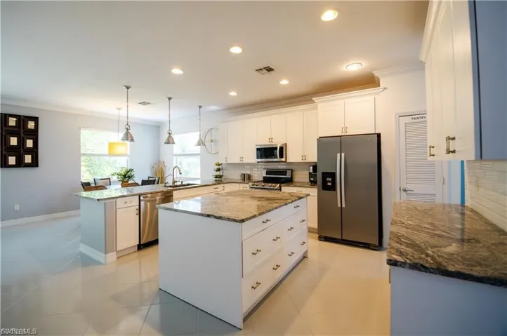 Kitchen featuring dark stone countertops, stainless steel appliances, ornamental molding, hanging light fixtures, and white cabinets