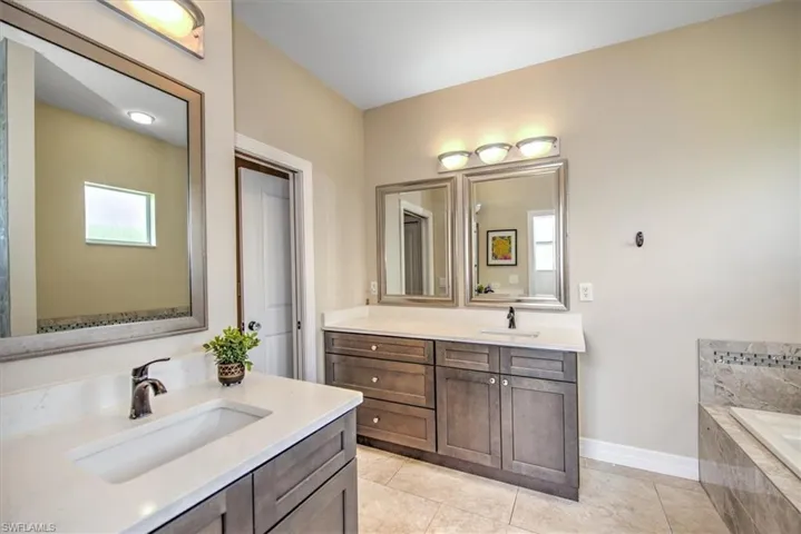 Bathroom with vanity, tile patterned floors, and tiled tub