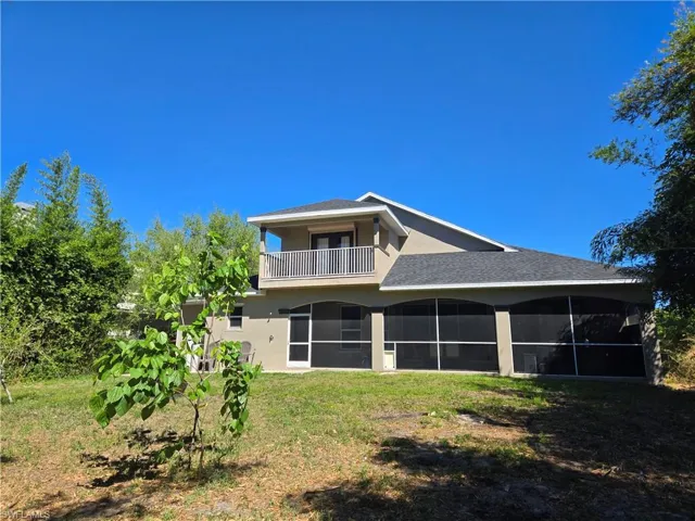Rear view of property featuring a balcony, a yard, a sunroom, and stucco siding