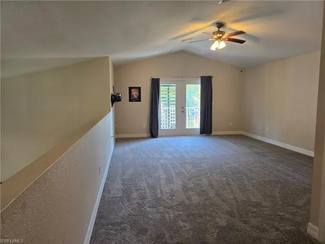 Carpeted spare room with lofted ceiling, a ceiling fan, and baseboards