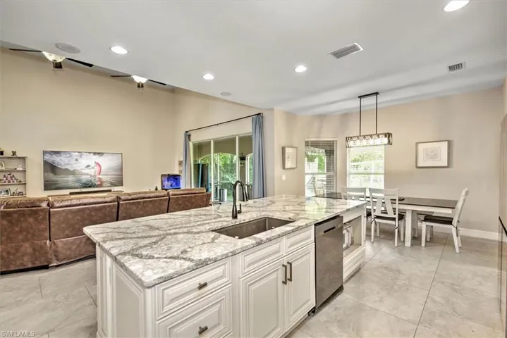 Kitchen with dishwasher, sink, hanging light fixtures, light stone countertops, and white cabinetry