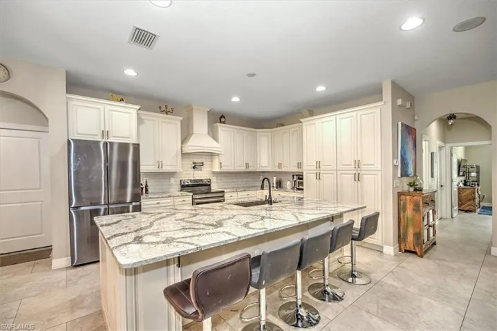 Kitchen with premium range hood, light stone countertops, an island with sink, and appliances with stainless steel finishes