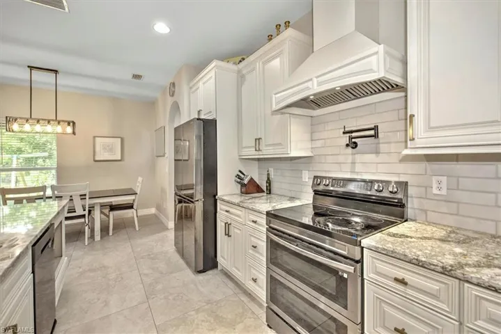 Kitchen with light stone countertops, white cabinetry, premium range hood, and stainless steel appliances