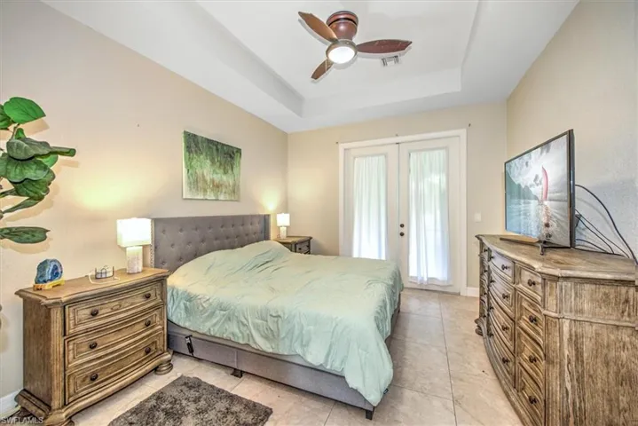 Tiled bedroom with french doors, access to outside, a raised ceiling, and ceiling fan
