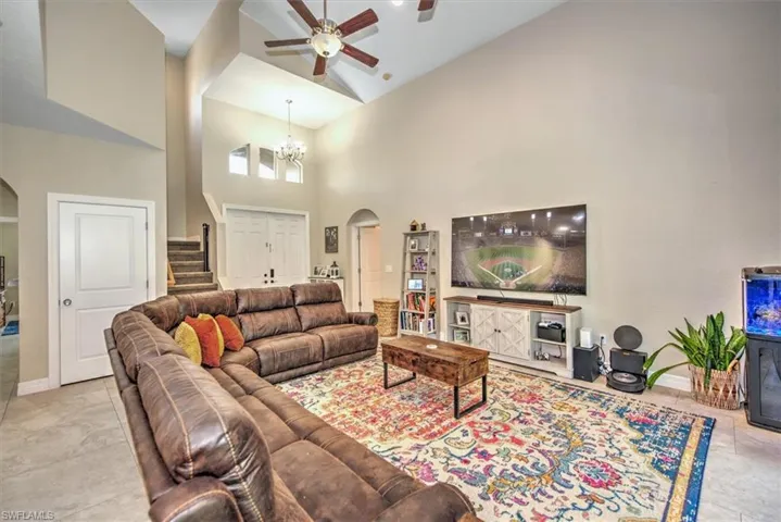 Tiled living room with ceiling fan with notable chandelier and high vaulted ceiling