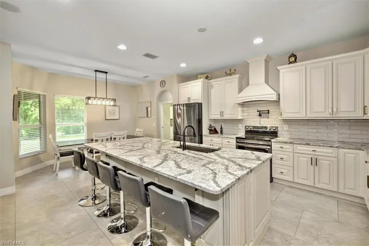 Kitchen featuring appliances with stainless steel finishes, premium range hood, light stone counters, sink, and an island with sink
