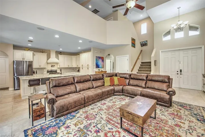 Tiled living room with ceiling fan with notable chandelier and a towering ceiling