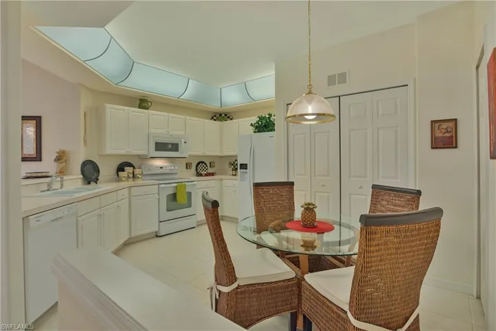 Kitchen with white appliances, light countertops, white cabinets, light tile patterned flooring, and decorative light fixtures
