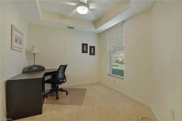Office with a tray ceiling, light colored carpet, and ceiling fan