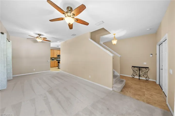 Unfurnished living room with light carpet, ceiling fan, stairs, and light tile patterned floors