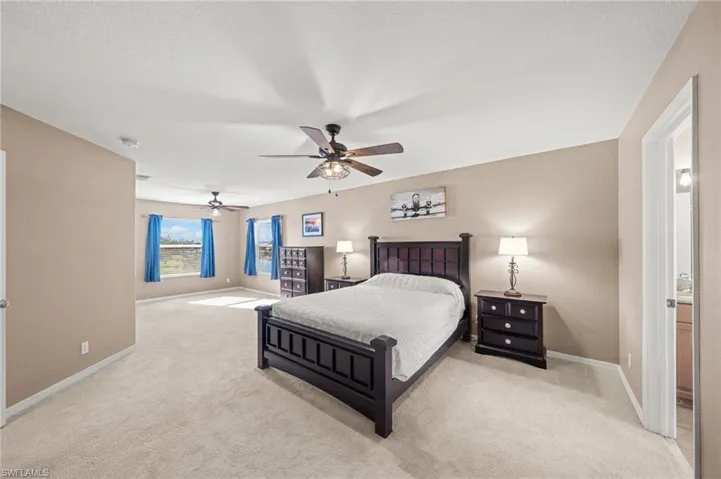 Bedroom featuring light colored carpet, a ceiling fan, and connected bathroom