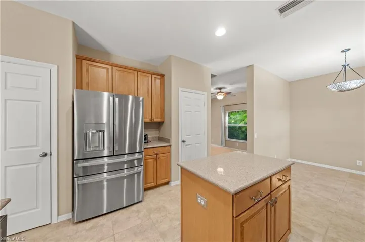 Kitchen featuring stainless steel fridge, pendant lighting, light stone counters, a center island, and recessed lighting