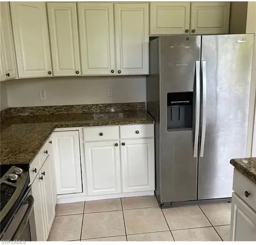 Kitchen featuring stainless steel appliances, white cabinetry, light tile patterned floors, and dark stone counters