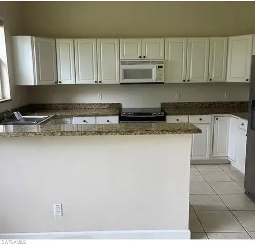 Kitchen featuring white cabinetry, stove, light tile patterned floors, and dark stone countertops