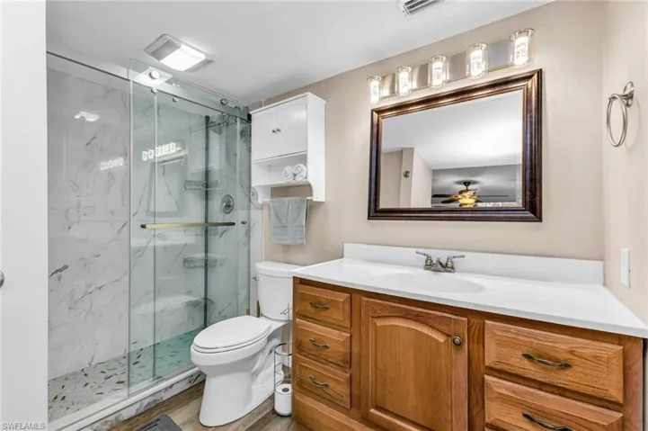 Full bath with vanity, a marble finish shower, and wood finished floors