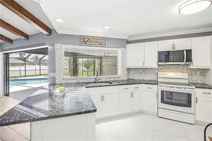 Bright kitchen featuring white cabinetry, dark stone countertops, and a white subway tile backsplash