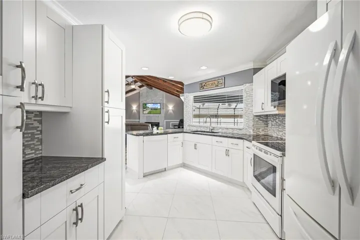 Modern kitchen featuring white cabinetry, dark granite countertops, a patterned tile backsplash, white appliances, and tiled flooring