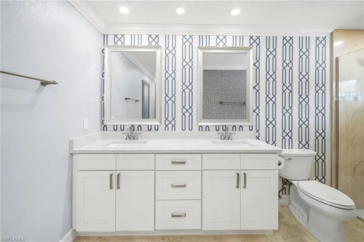 Dual vanity featuring white shaker cabinetry, light-toned countertops, and two framed mirrors