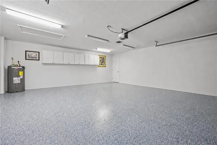 Spacious garage featuring a speckled epoxy floor, extensive overhead white cabinetry for storage, and bright overhead fluorescent lighting