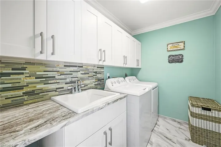 Laundry area featuring white shaker cabinetry, a utility sink with a chrome faucet, a patterned tile backsplash, and stone-look countertops