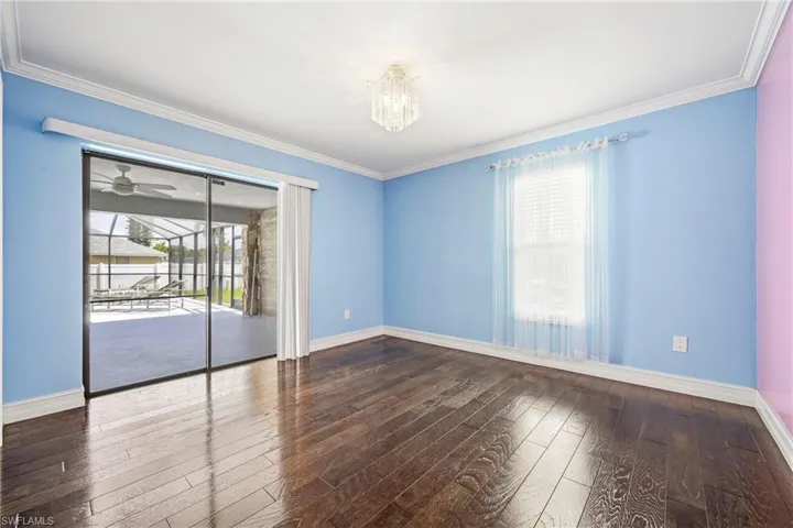 Spacious room featuring rich wood-finish flooring, crown molding, and an elegant chandelier