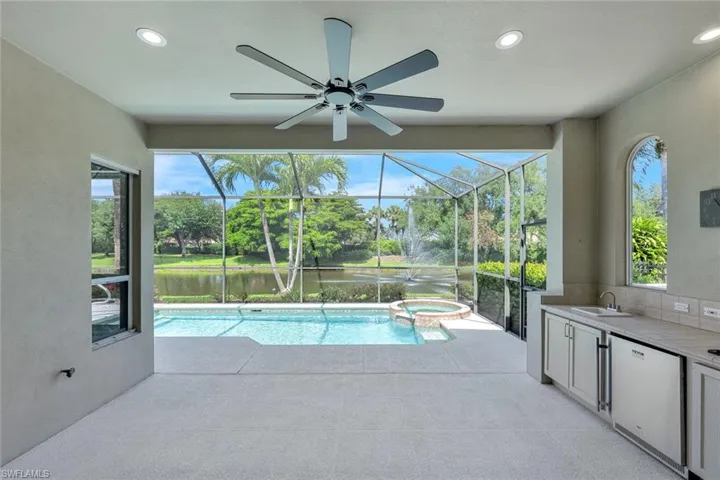 View of pool with a pool with connected hot tub, area for grilling, a lanai, a ceiling fan, patio and outdoor kitchen area with new stainless stell fridge.