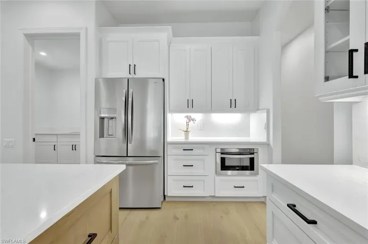 Kitchen with stainless steel appliances, light countertops, light wood-style floors, glass insert cabinets, and white cabinets