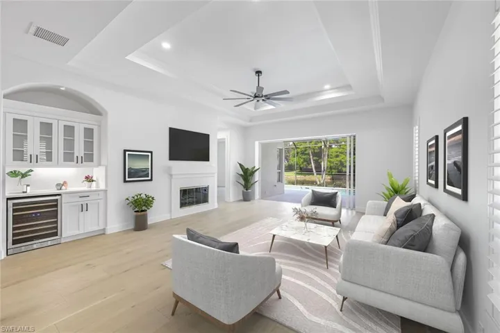 Staged living room featuring wine cooler, a tray ceiling, light wood finished floors, wet bar, and a ceiling fan