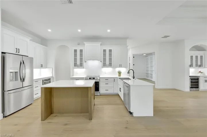 Kitchen featuring stainless steel appliances, wine cooler, arched walkways, a peninsula, and recessed lighting