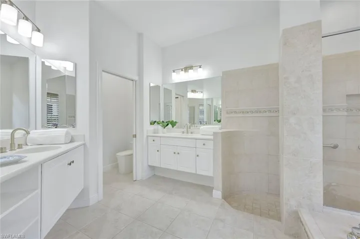 Primary bathroom with walk in shower, two vanities, and tile patterned flooring