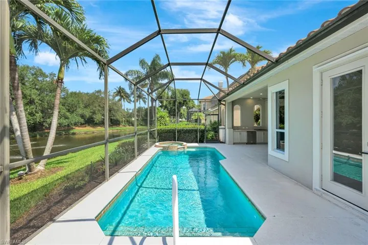 View of pool with a patio area, a pool with connected hot tub, a water view, and glass enclosure