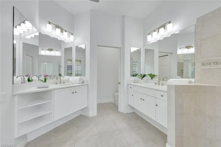 Primary bathroom with tile patterned floors, two vanities, and tiled shower
