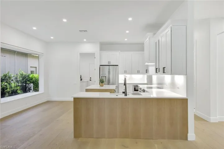 Kitchen featuring stainless steel fridge, light countertops, light wood finished floors, white cabinetry, and recessed lighting