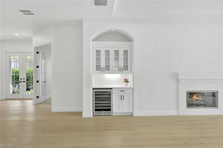 Indoor dry bar featuring beverage cooler, light wood finished floors, a glass covered fireplace, recessed lighting, and french doors
