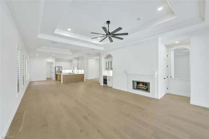 Unfurnished living room with a raised ceiling, arched walkways, a lit fireplace, a ceiling fan, and light wood-type flooring