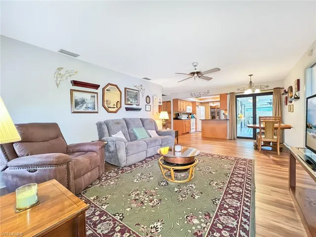 Living room featuring ceiling fan with notable chandelier and light wood-type flooring