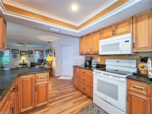 Kitchen with kitchen peninsula, white appliances, ceiling fan, light hardwood / wood-style flooring, and dark stone countertops