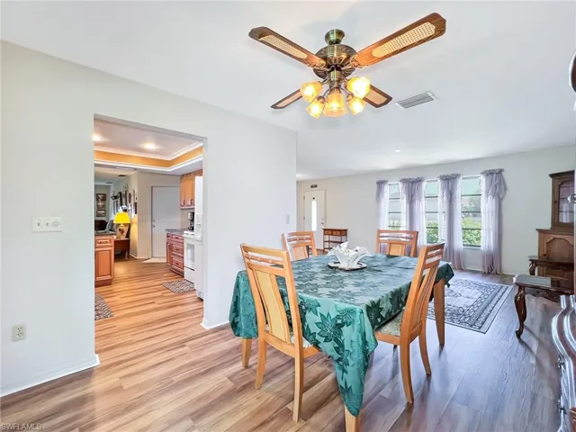 Dining space with light wood-type flooring, a raised ceiling, and ceiling fan